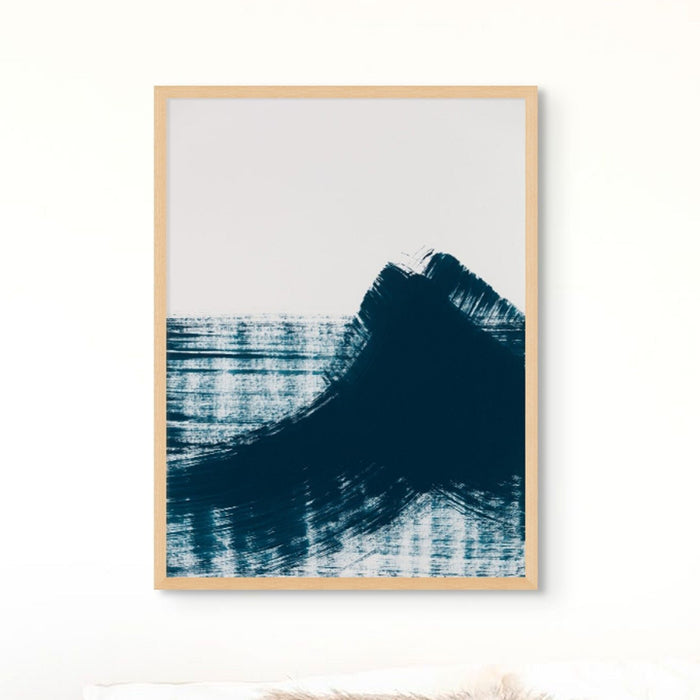 A framed abstract art print featuring swirls of dark blue and black on a light background, resembling ocean waves. The art print is shown on a white wall.