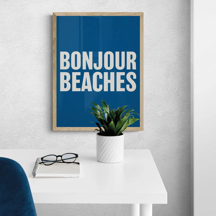 A colourful typography art print with the text 'BONJOUR BEACHES' in bold white letters on a navy blue background, framed on the wall in office.