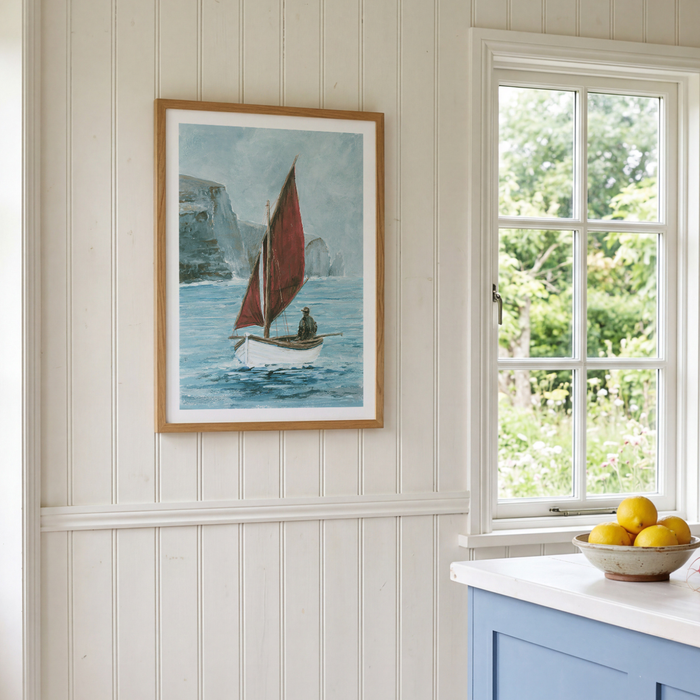 Framed artwork of a sailboat on a wall next to a window with a view of greenery.