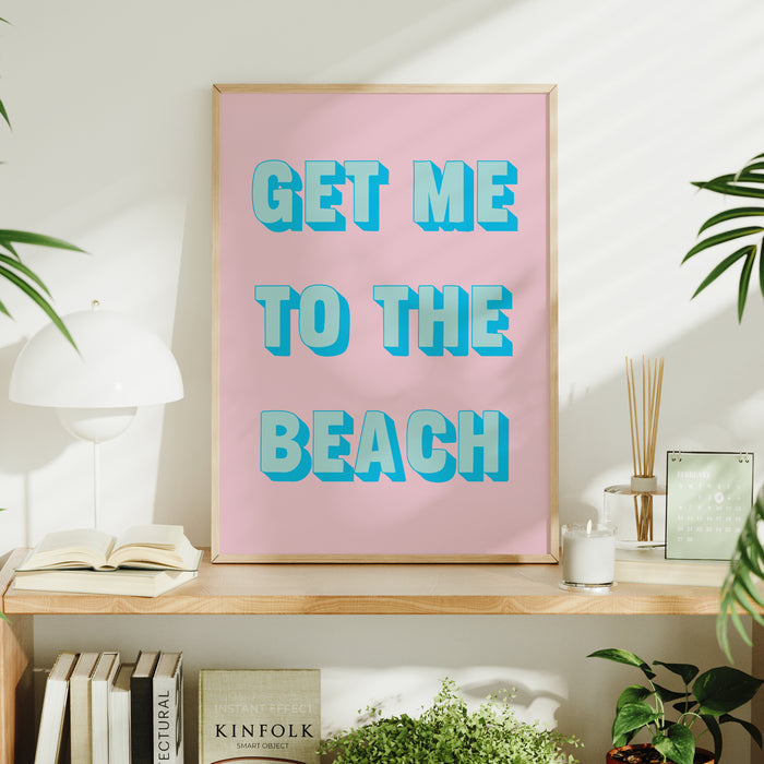Framed coastal artwork with 'GET ME TO THE BEACH' text on a pink background, displayed on a shelf.