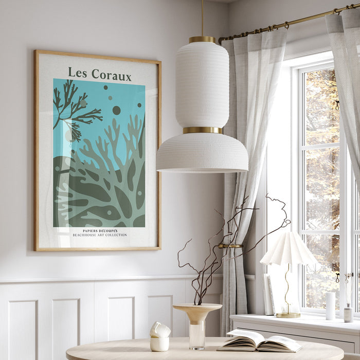 A framed coral art print in a dining room with a round table, chairs, and a window with curtains.