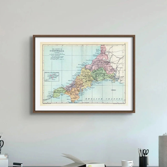 A vintage map print of Cornwall featuring different shades of colours for various regions, with a black frame in an office.