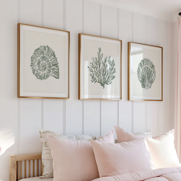 Set of 3 shell and coral art prints in natural wood frames, styled in a bright coastal interior bedroom with pink bedding, decorative pillows, and framed artwork on a white panelled wall.