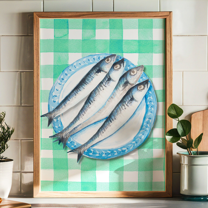 Framed artwork of fish on a plate. Sardines on a blue plate, placed on a green gingham tablecloth.