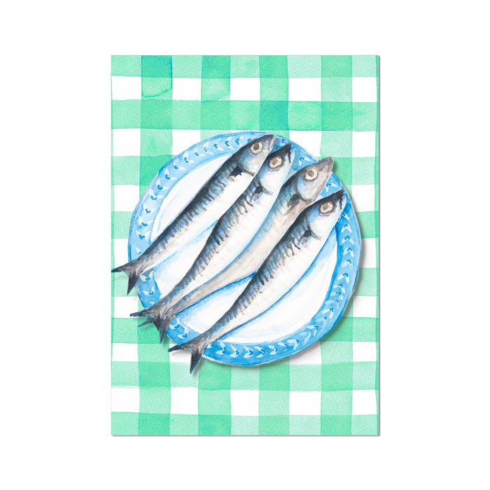 Hand-painted artwork of fish on a plate. Sardines on a blue plate, placed on a green gingham tablecloth.
