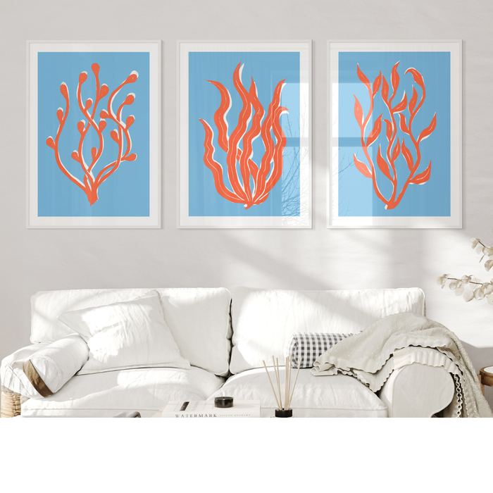 Three framed artworks of red coral on a blue background above a white sofa.