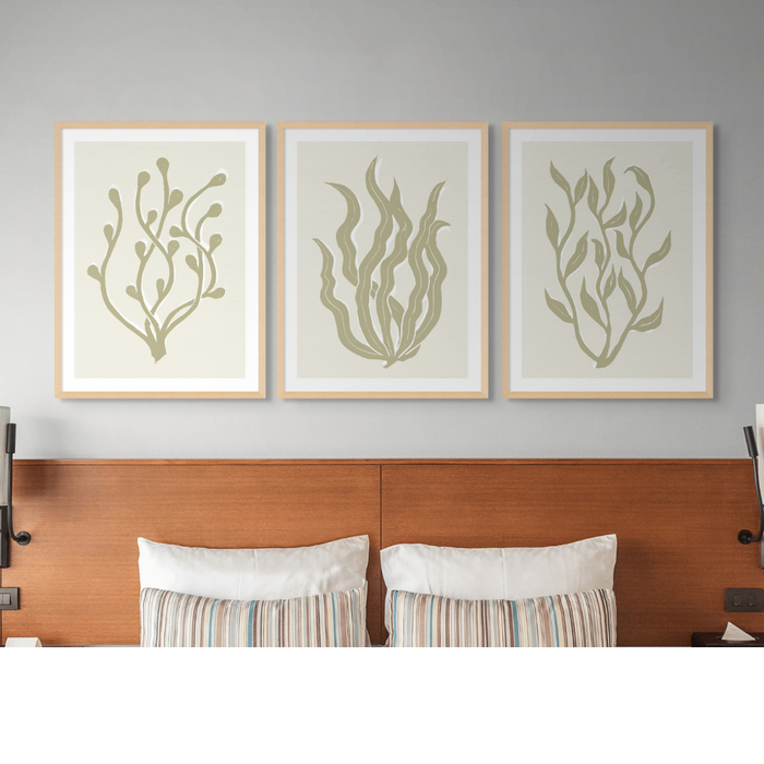 Three framed botanical prints above a wooden headboard with pillows.
