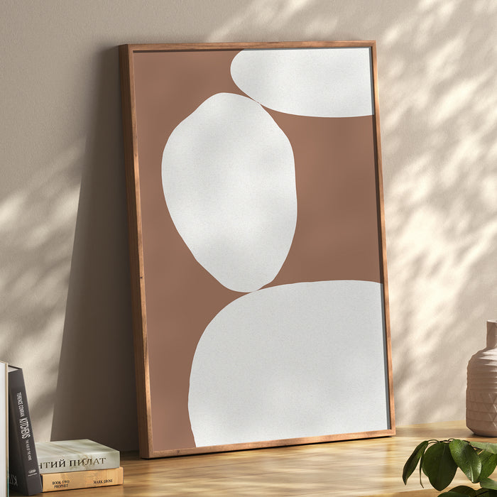 Abstract wall art print with white shapes on a brown background, displayed  on wooden desk. Abstract balancing stones print.