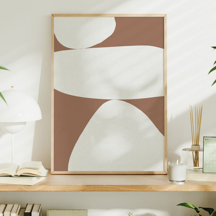 Abstract wall art print with white shapes on a mocha brown background, displayed on a wooden shelf. Abstract balancing stones print.