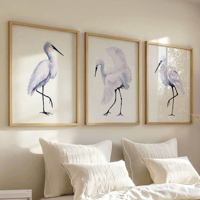 Set of 3 heron prints - Framed artwork of birds on a wall above a bed with pillows and blankets.
