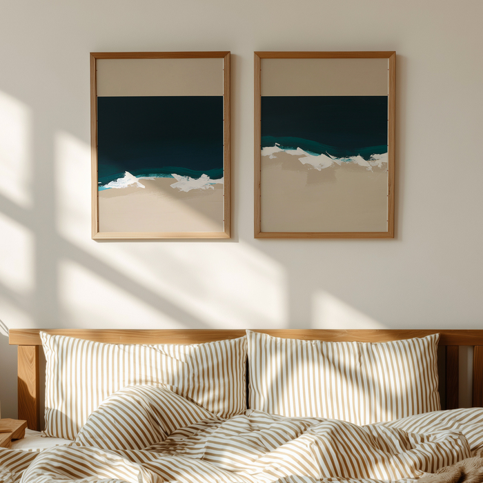Two framed coastal artworks of a beach scene on a wall above a bed with striped bedding.