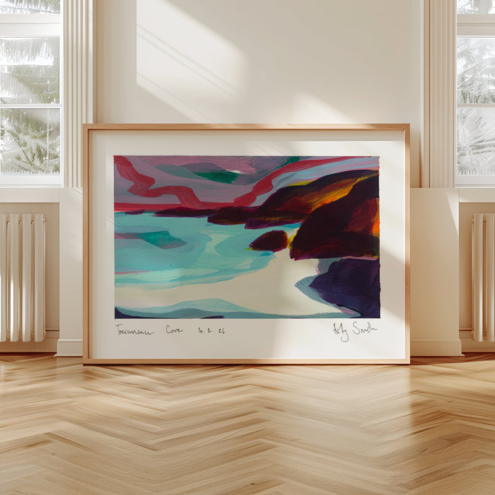 A framed abstract landscape painting leaning against a wall in a bright room with large windows and light wood flooring. The artwork features swirling teal, pink, purple, orange, and dark blue tones, enclosed in a light wood frame.