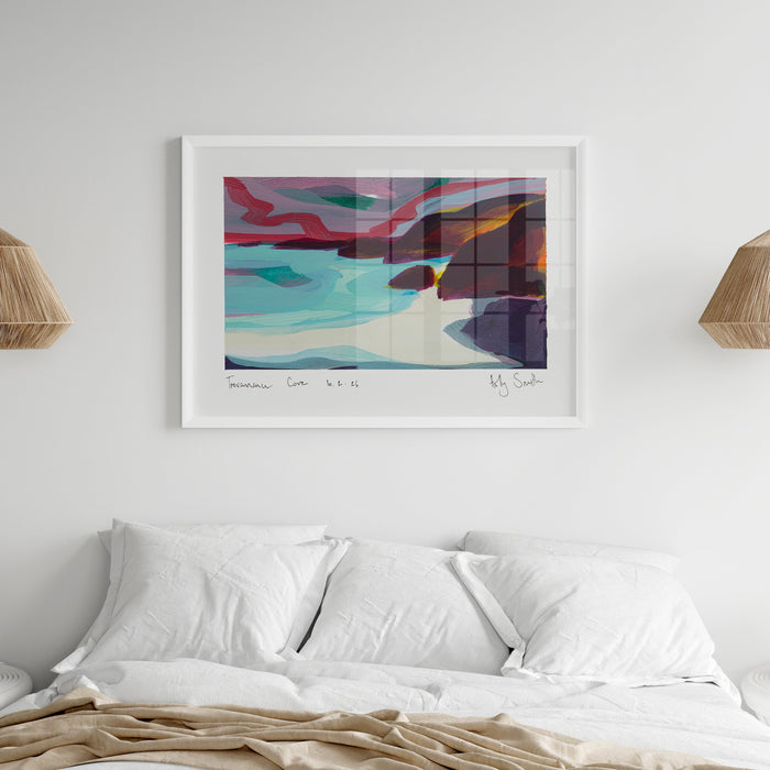 A framed abstract landscape painting leaning against a wall in a bright room with large windows and light wood flooring. The artwork features swirling teal, pink, purple, orange, and dark blue tones, enclosed in a light wood frame.