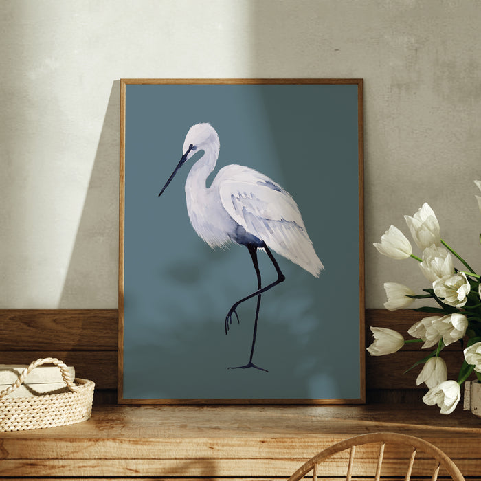 Framed artwork of a white bird on a blue background, displayed on a wooden surface with flowers and a basket.