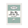 A framed art print featuring a vintage book cover art with the title 'You Me and the Sea' by Blu Skye, with a green background and a small illustration of a dolphin at the bottom.